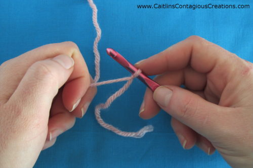 Pink yarn attached to crochet hook on blue background