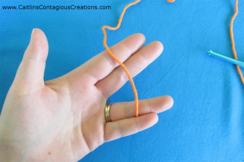 step 1 of magic ring tutorial. holding tail end of orange yarn between pinky and ring fingers
