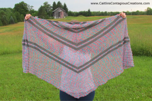 model holding finished shawl pattern up to show striped pattern followed by lacey portion of pattern.