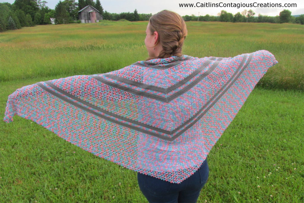 outstrrrretched arms with finished triangle shawl draped over with grassy background