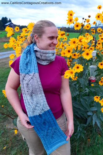 completed knotted cable scarf worn by model near yellow daisies